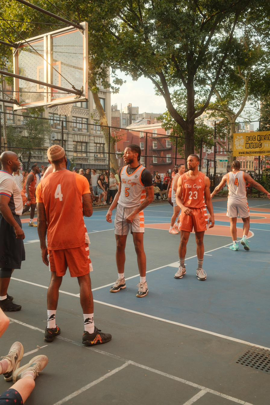 Players in orange and grey kit facing off on the West 4th Street basketball court at golden hour.