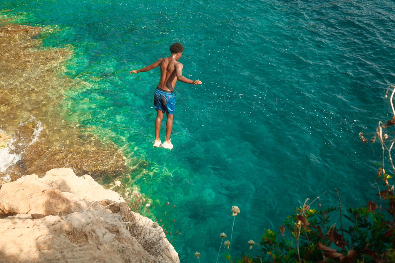 A boy suspended mid-air above turquoise water after jumping from a limestone cliff.