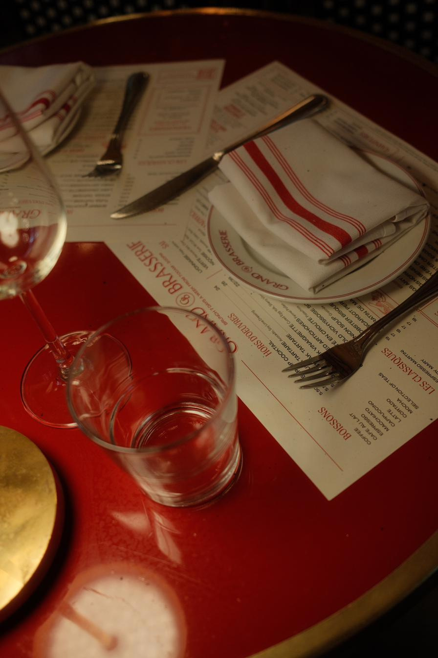 Menus, striped napkins and glassware laid across a lacquered red café table.