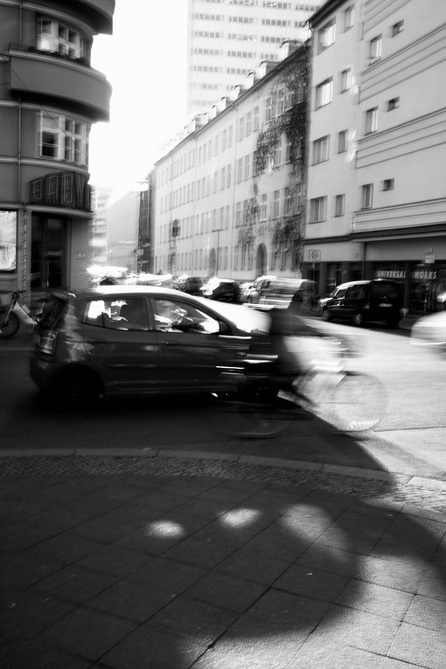 Black and white long exposure of a car and cyclist crossing a bright city junction.