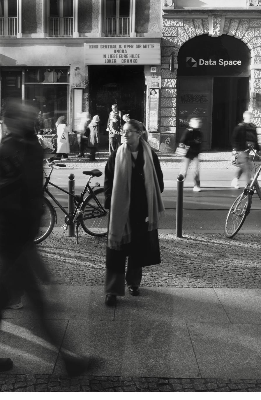 Black and white street scene outside a cinema, one woman still while passers-by blur.