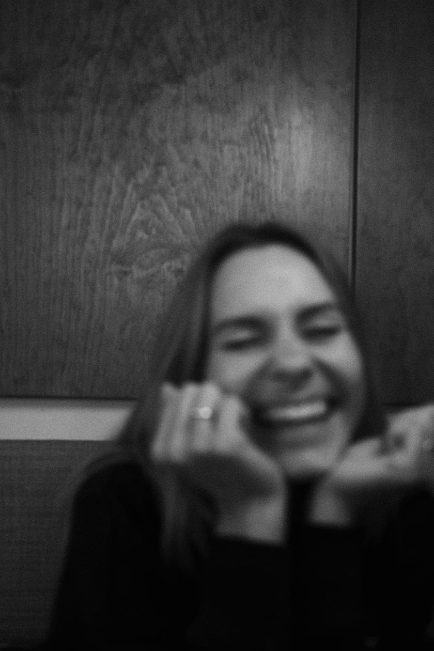 Soft black and white frame of a woman laughing, her hands raised to her face.