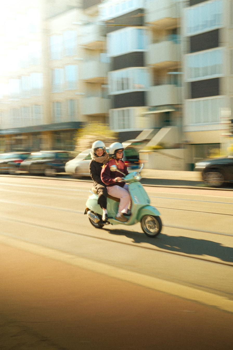 Two riders on a mint green scooter, panned so the street smears behind them.
