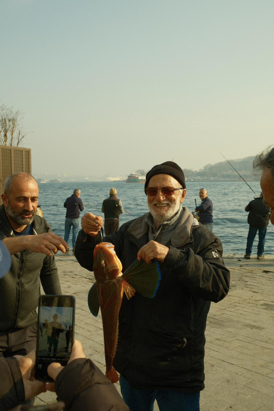 An older fisherman on the waterfront grinning as he fans out the fins of his catch.