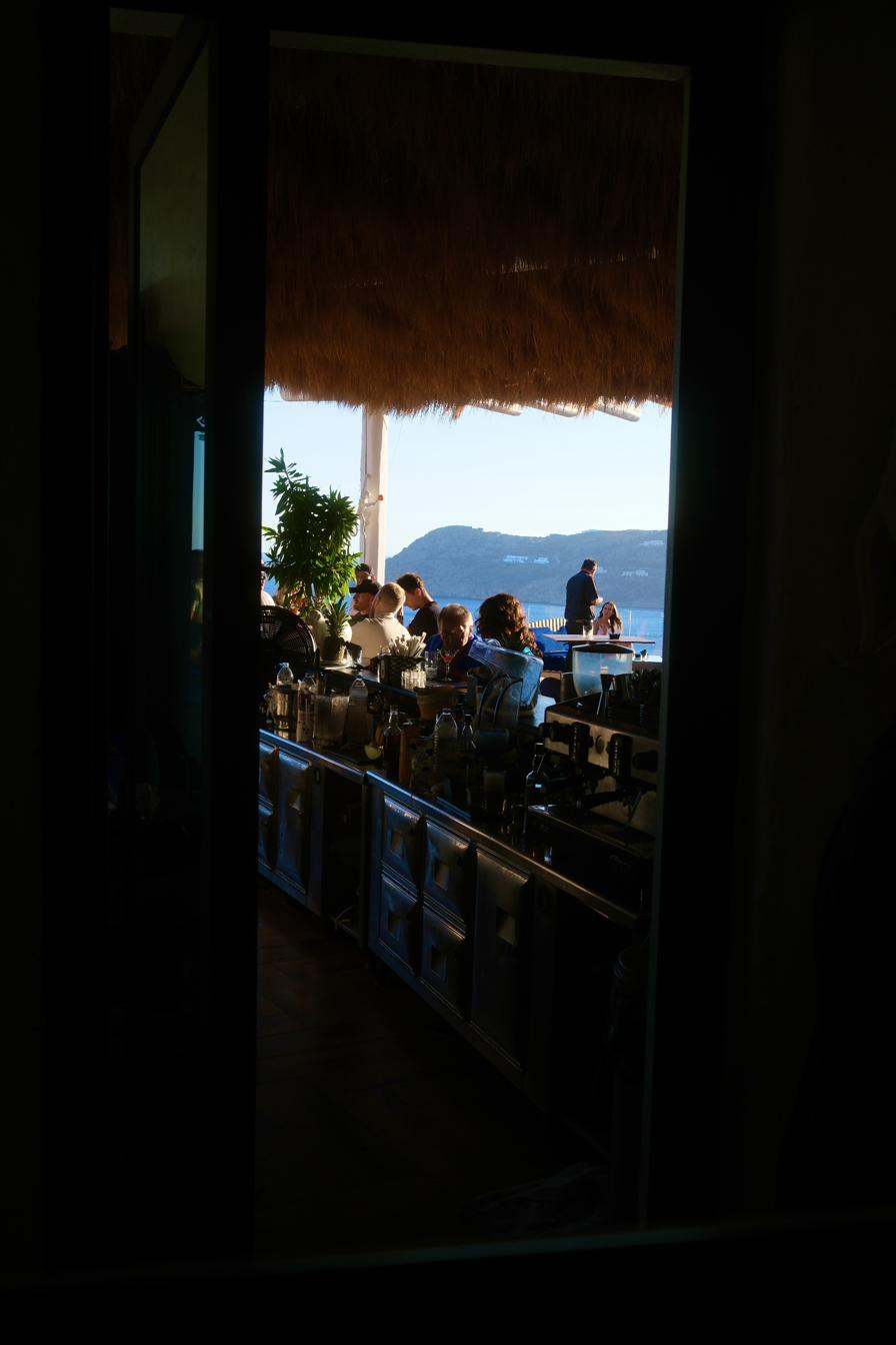 A dark doorway opening onto a bright terrace bar above the sea.